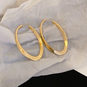 Detailed view of large gold irregular oval hoop earrings on white textured paper