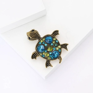 Detailed close-up of retro turtle brooch with blue and green rhinestones on white block