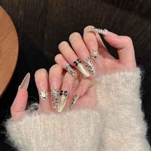 Handmade almond press-on nails with black tweed patterns, bows, and pearls on a plush sweater