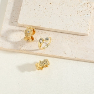 Golden 14K plated flower rings with zircon accents on a neutral textured background