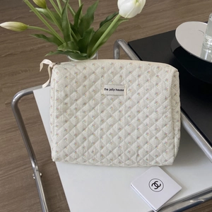 Detail of white quilted floral makeup bag with brand label and ribbon zipper pull
