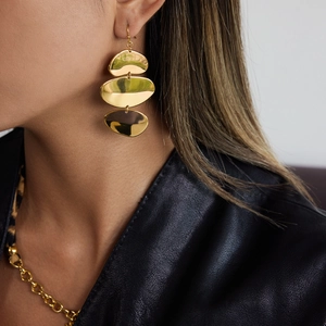 Détail de boucles d'oreilles ovales dorées à trois couches portées avec une veste en cuir