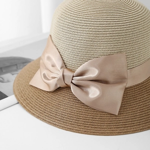 Close-up of elegant two-tone straw hat featuring a champagne gold satin bow accent