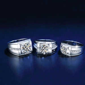 Close-up of three silver men's rings with square faces and central gemstones on blue surface