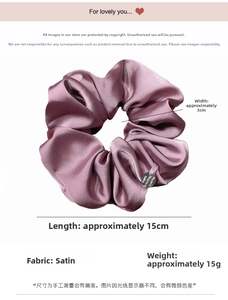Detail of burgundy satin hair scrunchie with smooth silk texture and metallic brand tag