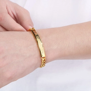 Detail of gold curb chain bracelet for men with Roman numeral engraved curved plate