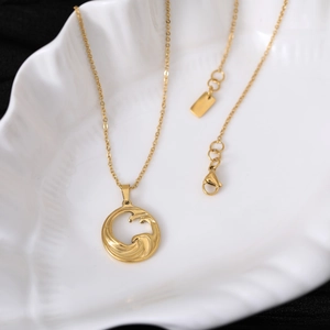 Detailed view of a gold wave pendant necklace displayed on a white shell stand