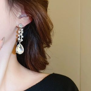 Dettaglio di un orecchino lungo a goccia d'argento con cristalli brillanti su modella