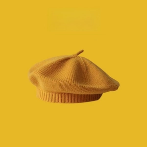Close-up of bright yellow knitted beret hat featuring a top stem and ribbed edge finish