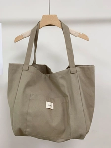 Minimalist canvas tote bag with contrast stripes and khaki front pocket on hanger