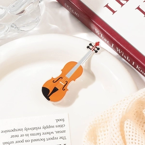 Close-up of a small orange acrylic guitar hair clip on a white decorative dish