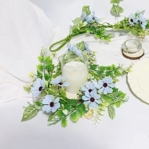 Close-up of light blue daisy candle ring with lush green fern leaves on white tablecloth