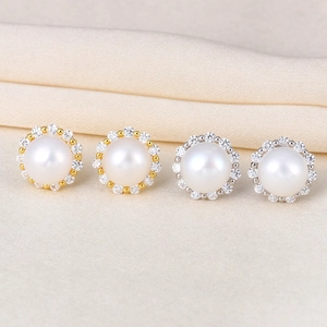 Detail of silver and gold pearl halo earrings with zircon accents on beige silk fabric