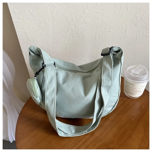 Detail of light green crescent nylon bag with small round coin purse charm on a wood table