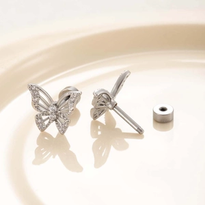Silver butterfly cartilage earrings with clear cubic zirconia on a beige plate