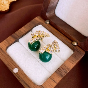 Macro shot of gold zircon gourd earrings with emerald green beads in a wooden box
