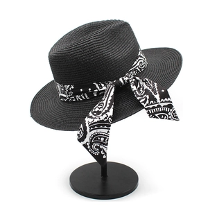 Detail of black straw Panama hat featuring a paisley print ribbon bow on a display stand