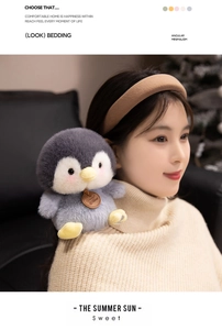 Cute plush penguin toy with soft grey and white fur sitting on a person's shoulder