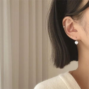 Detail of silver heart drop earring with cubic zirconia on model with beige knitwear