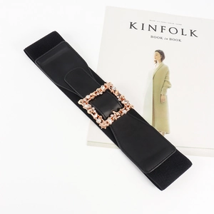 Detail view of black elastic waist belt with a gold rhinestone square buckle on a book