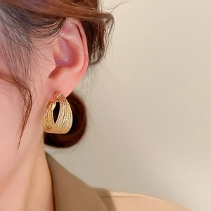 Detailed close-up of chunky gold layered braided earrings worn by a fashion model