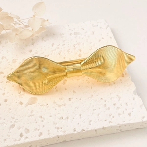 Golden alloy bow hair clip with textured surface on white decorative stone