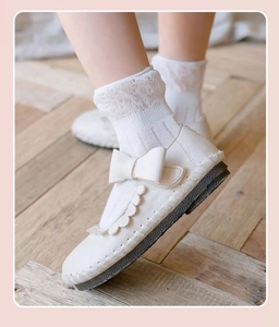 Close-up of white Mary Jane shoes with bow and lace trim on vintage wooden floor