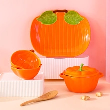 Creative orange pumpkin-shaped ceramic tableware set with green leaf lid on pink background