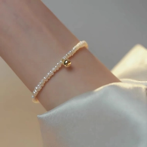 Elegant pearl bracelet with gold bead on wrist over silk fabric background