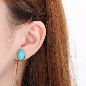 Close-up of elegant oval turquoise stud earring with golden floral lace border on ear