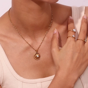 Detailed shot of golden moon pendant necklace and minimalist zircon rings set on a model