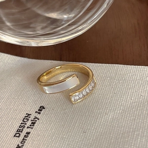 Detailed shot of golden open ring with white inlay and sparkling stones on beige fabric