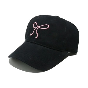Close-up of pink ribbon bow embroidery on a black cotton baseball cap with curved brim
