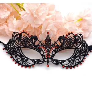 Detail of black lace masquerade mask with red rhinestones and intricate floral vine patterns