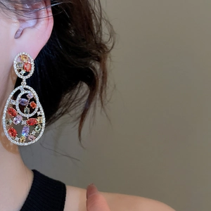 Close-up of elegant gold drop earrings with multi-colored gemstones on model