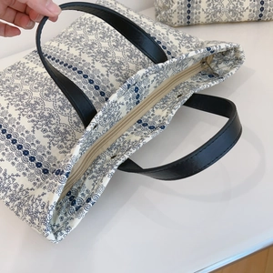 Detail of floral canvas tote bag showing black leather handles and zipper closure