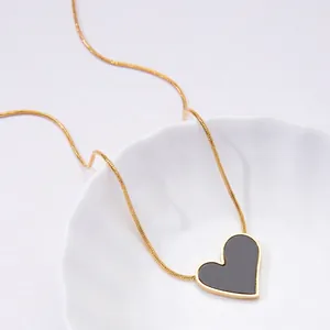Detailed close-up of a heart pendant on a gold snake chain in a white ceramic dish