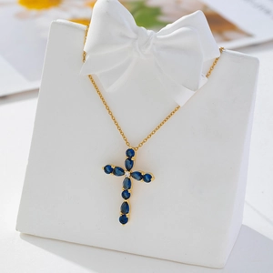 Macro shot of gold cross pendant featuring drop-shaped blue gems on a display stand