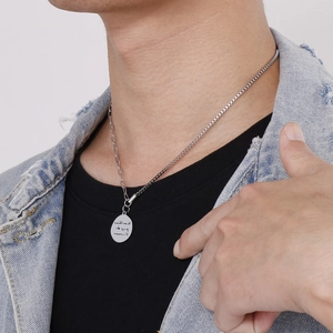 Silver round pendant necklace with Persian engraving worn over a black t-shirt and denim