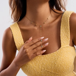 Detail view of a 18K gold-plated Y-shaped necklace with small turquoise beads on a model
