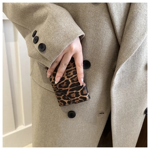 Detail of leopard print faux leather envelope wallet held against a beige coat background