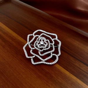 Détail de la broche rose argentée sertie de zircons sur fond de bois et de satin