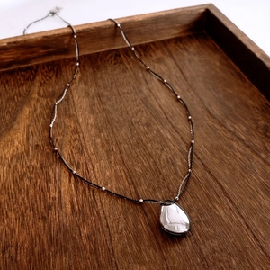 Close-up of a mirror-polished silver teardrop pendant on a mixed cord and bead chain