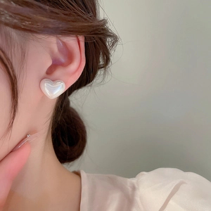 Macro shot of elegant heart-shaped pearl earrings worn on ear with soft satin blouse