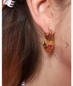 Close-up of heart-shaped gold earring with pink gemstone and colorful micro-inlay