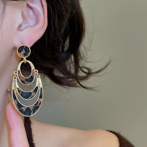 Detail of layered gold leopard print earrings worn by a model in warm lighting