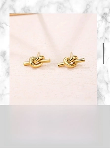 Macro shot of gold-plated stainless steel knot earrings on light pink textured surface