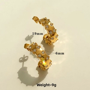 Detail of C-shaped gold-plated hoop earrings with textured finish and zircon inlays