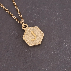 Close-up of golden hexagonal letter J pendant with embossed detail and sandblasted texture