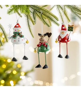 Three metal Christmas ornaments with Santa, snowman and elk hanging on a pine tree branch